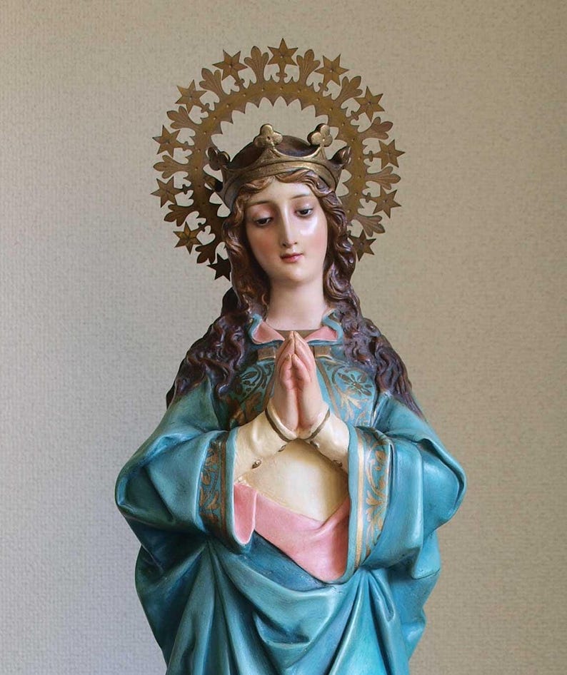 K&ouml;nnte beinhalten: Statue einer Frau mit Krone und Sternen-Heiligenschein. Sie tr&auml;gt ein blaues Gewand mit goldenen Verzierungen und hat die H&auml;nde zum Gebet gefaltet. Die Statue hat einen ruhigen Ausdruck.