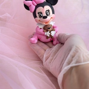 Sugar figurine of a mini baby in pink with a pink bow and holding a teddy bear.