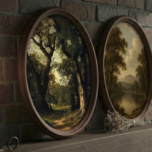 Op de afbeelding: Twee ovale landschapsschilderijen met bruine houten frames. Eén toont een bospad, de andere een rivierlandschap. Een brandende kaars in een zwarte kandelaar en droogbloemen zijn ook aanwezig.