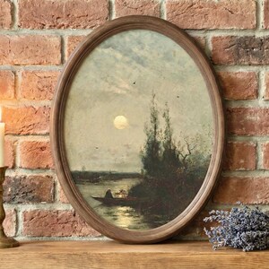 May include: Oval framed landscape painting depicting a moonlit river scene with a boat. The artwork is in a wooden frame. A lit candle in a brass holder and a bundle of lavender are on a wooden surface in front of a brick wall.