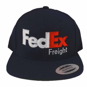 May include: A navy blue baseball cap with a white and red embroidered FedEx Freight logo.