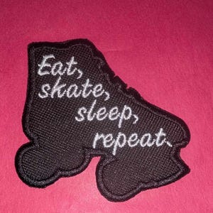 May include: Black embroidered patch shaped like a roller skate with white text that reads "Eat, skate, sleep, repeat."