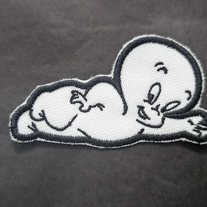 May include: White embroidered patch of a cartoon ghost lying on its side with its arms crossed. The ghost has a black outline and a mischievous expression.
