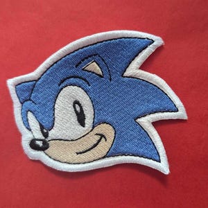 May include: A blue and white embroidered patch of Sonic the Hedgehog, a popular video game character.