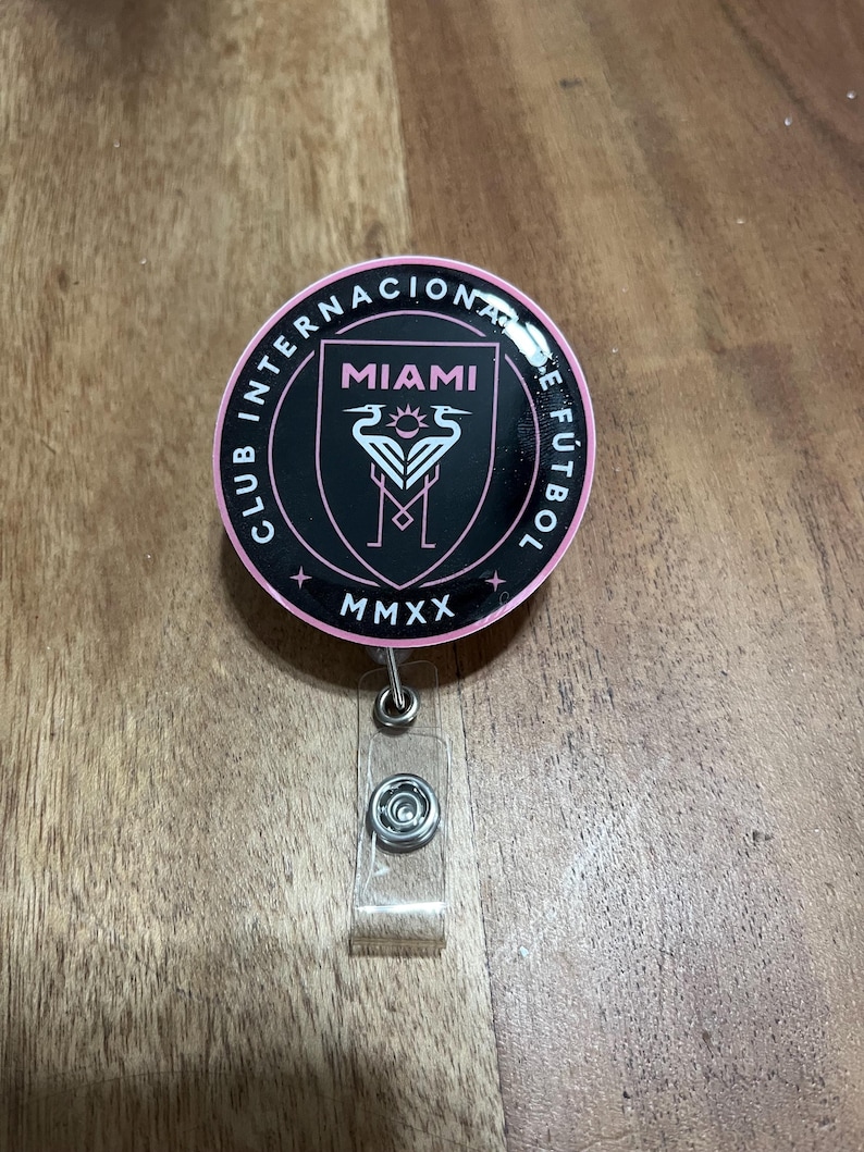 May include: A black and pink round badge with the text "Club Internacional de F&uacute;tbol Miami MMXX" and a pink flamingo logo.