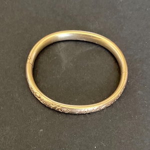 May include: A gold bangle bracelet with a delicate floral design.