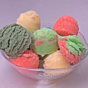 May include: A clear glass bowl filled with colorful ice cream scoops. The scoops are in shades of green, yellow, pink, and red.