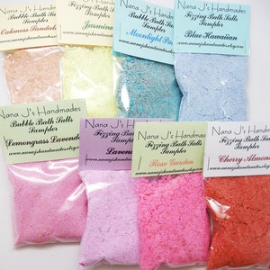 May include: A collection of colorful bath salt samplers in clear plastic bags. Flavors include Oakmoss Sandal, Jasmine, Moonlight Paradise, Blue Hawaiian, Lemongrass Lavender, Lavender, Rose Garden, and Cherry Almond. Each bag has a label with the product name.