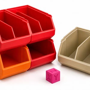 Puede incluir: Un conjunto de cajas de almacenamiento apilables en rojo y naranja, junto a una caja beige separada y un pequeño cubo rosa con las letras X, Y y Z en sus caras. Estos contenedores de plástico tienen frentes abiertos y divisores internos.