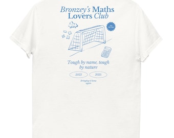 May include: White t-shirt with a light blue graphic design. The design includes the text "Bronzey's Maths Lovers Club", a soccer goal, a calculator, and the phrase "Tough by name, tough by nature".