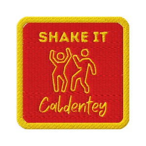 May include: Embroidered patch with a red background and yellow border. The patch features the text "SHAKE IT" above two stick figures dancing, and the word "Caldentey" below. The text and figures are in yellow.