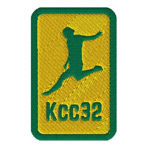 Puede incluir: Parche bordado con borde verde y centro amarillo. El centro presenta una silueta verde de una persona saltando, con el texto "KCC32" debajo. El parche tiene una apariencia texturizada.
