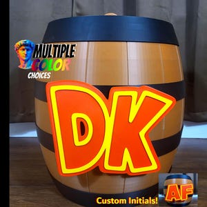 Puede incluir: Un recipiente en forma de barril con acabado de madera marrón y bandas negras. Las letras "DK" en naranja con contorno amarillo se muestran prominentemente en la parte delantera. También se ve el texto "Multiple Color Choices" y "Custom Initials!"