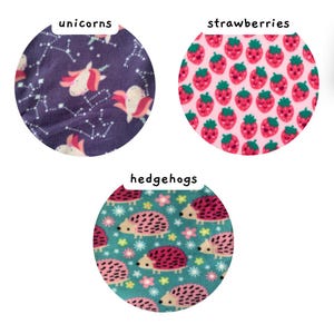 May include: Three circular fabric swatches featuring distinct patterns. The first is purple with unicorns and white constellations. The second is pink with smiling strawberries. The third is teal with pink hedgehogs and small flowers.