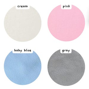 May include: Four circular fabric swatches arranged in a grid. The top left is cream, the top right is pink, the bottom left is baby blue, and the bottom right is gray. Each swatch has a small white label above it with the corresponding color name.