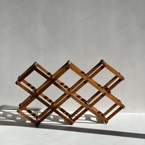 May include: A wooden wine rack with a diamond-shaped design. The rack is made of light brown wood and can hold multiple bottles. The rack is designed to be collapsible and is suitable for home use.