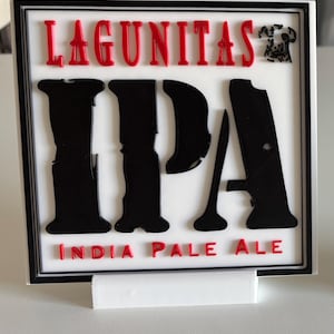 May include: A square sign with the words "LAGUNITAS IPA INDIA PALE ALE" in red and black. The sign has a white background and a black border. A small dalmatian dog graphic is in the upper right corner.