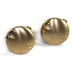 May include: A pair of round gold-toned cufflinks featuring a brushed metal finish. Each circular cufflink is decorated with two small, engraved leaf motifs positioned on opposite sides of the face, providing a subtle texture to the surface.