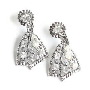 May include: A pair of silver-toned clip-on earrings. Each earring features a floral-shaped top with a large, round clear stone. The lower portion is a fan-shaped design with clear, round and marquise-cut stones.