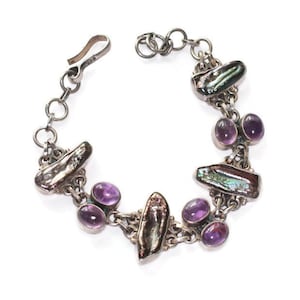 May include: A silver chain bracelet featuring alternating oval purple amethyst gemstones and elongated, iridescent dark shell segments. The bracelet includes a silver hook clasp and a series of circular links, with a small 925 stamp visible.
