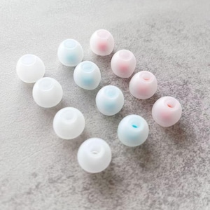 May include: A collection of twelve small, spherical, semi-translucent silicone earbud tips arranged in a grid. The tips feature a smooth, matte finish with a hollow centre, displaying a soft colour palette of white, pale blue, and light pink.