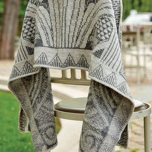 Puede incluir: Una manta de punto gris y blanca con un patrón geométrico. La manta está drapeada sobre una silla.