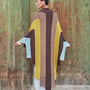 May include: A woman wearing a colorful, striped knit wrap. The wrap features vertical stripes in shades of brown, yellow, and blue. The garment is long and flowing, with sleeves that extend to the elbows. The background is a weathered wooden door.