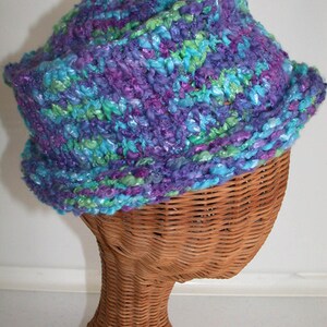 May include: A purple, blue, and green knitted hat on a wicker hat form.