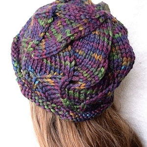May include: A knitted hat in shades of purple, green, and brown with a cable knit pattern.