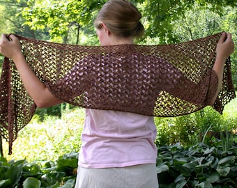 May include: A brown crocheted shawl with a lacy pattern. The shawl is draped over the shoulders of a person wearing a pink shirt and white trousers.