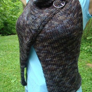 May include: A brown, blue, and grey knitted vest with a metal ring closure. The vest is open in the front and has a draped look.