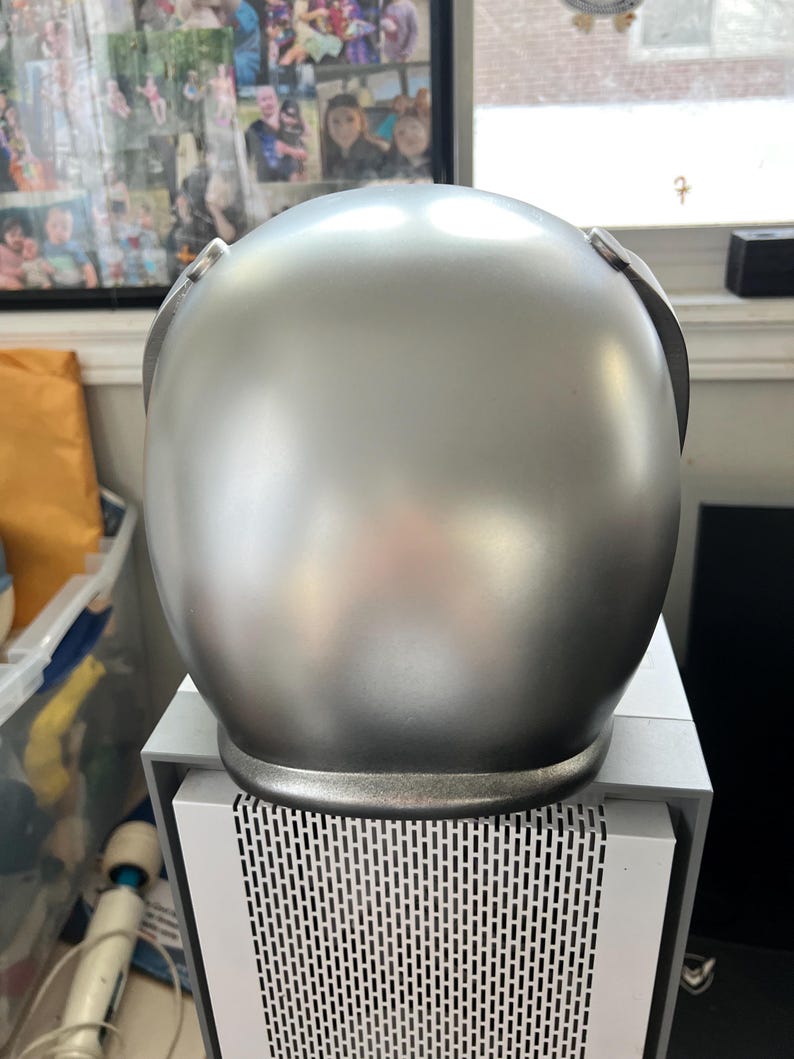 May include: A silver helmet with a smooth, shiny finish. The helmet has a rounded shape and a slightly raised rim around the bottom edge.