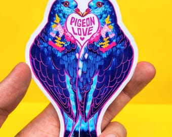 Könnte beinhalten: Ein Aufkleber mit zwei blauen und rosa Tauben, die sich gegenüberstehen, mit einem rosa Herzen, auf dem in weißen Buchstaben "Pigeon Love" steht.