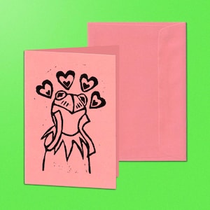 May include: A pink greeting card featuring a black illustration of a frog with hearts above its head, alongside a pink envelope. The frog is depicted in a simple, cartoon style. The background is a bright green.