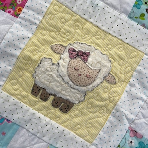May include: A white and yellow patchwork quilt with a white lamb applique in the center. The lamb has a pink bow and a brown nose. The quilt is made of various fabrics with different patterns, including polka dots, stripes, and floral prints.