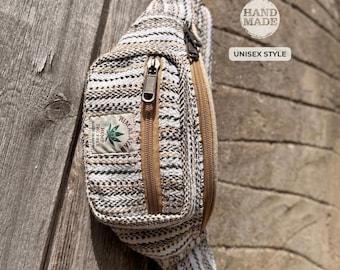 May include: A hand-made, unisex style fanny pack with a woven, striped pattern in shades of beige, brown, and white. The bag features two zippered compartments with brown zippers and a small patch that reads "Himalaya Hemp THC Free".