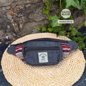 May include: A grey hemp fanny pack with a herringbone pattern and a front zipped pocket. The pack has a colourful woven design on the sides and a label reading "Himalayan Hemp." The text "Hand Made" and "Unisex Style" are also visible.