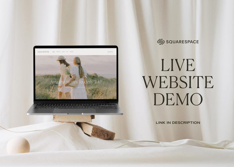 May include: A laptop computer displaying a website with the text "Amazing Stories Tenderly Told" on the screen. The laptop is on a wooden platform and a white ball is in the foreground. The background is a white fabric backdrop with the text "SQUARESPACE LIVE WEBSITE DEMO LINK IN DESCRIPTION" in black.