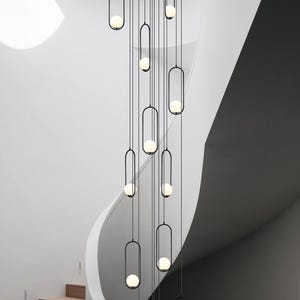 May include: A modern black metal chandelier with multiple globe-shaped light bulbs hanging from a white ceiling in a staircase.