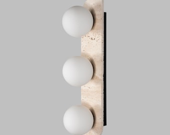 May include: A wall-mounted light fixture with three white globe-shaped light bulbs. The fixture is made of a light brown stone with a black metal backing.