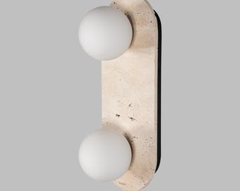 May include: Modern wall sconce featuring a light beige, oblong stone base with two spherical, white light fixtures. The sconce has a black backing and is designed for indoor lighting.