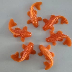 May include: Six orange rubber goldfish toys arranged in a circle on a white background.