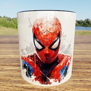 Puede incluir: Una taza de cerámica blanca con una vibrante ilustración estilo acuarela del superhéroe Spider-Man. El diseño muestra la icónica máscara roja y azul del personaje con detalles de telaraña en negro sobre un fondo blanco limpio.