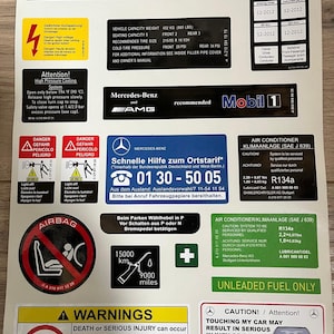Puede incluir: Un conjunto de pegatinas de advertencia e información para un vehículo Mercedes-Benz. Incluye advertencias de seguridad sobre airbags, presión de neumáticos y combustible sin plomo. Presenta los logotipos de Mercedes-Benz y AMG.