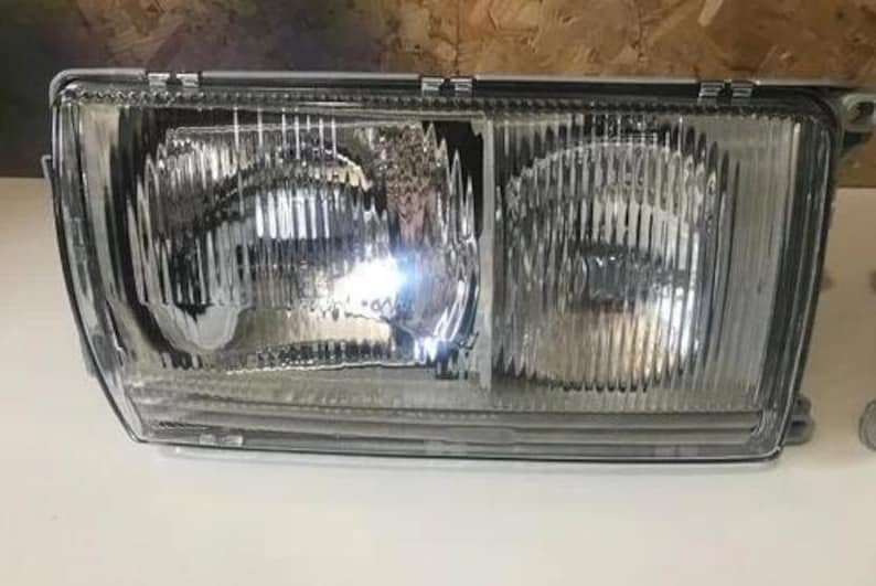 A clear headlight of a vehicle, with a reflective surface that allows light to pass through.