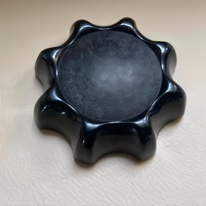 Puede incluir: Un pomo negro brillante con un diseño en forma de estrella. El centro del pomo es una superficie circular texturizada. El pomo se utiliza probablemente para ajustar o apretar un mecanismo.