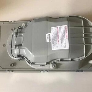 a grey plastic object, possibly a part of a vehicle, with a warning label on it.