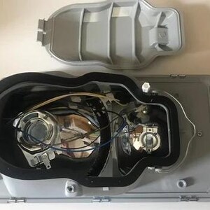 the interior of a vehicle, specifically the front headlight assembly, with various components and wiring visible.