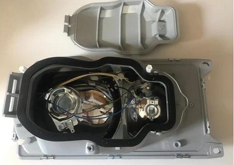 the interior of a vehicle, specifically the front headlight assembly, with various components and wiring visible.