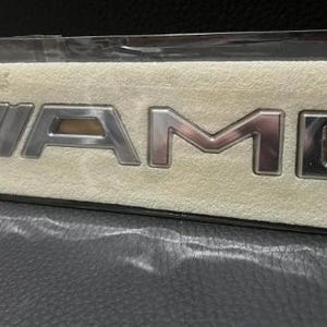 a close-up view of a silver and gold Mercedes-Benz logo on a beige background.